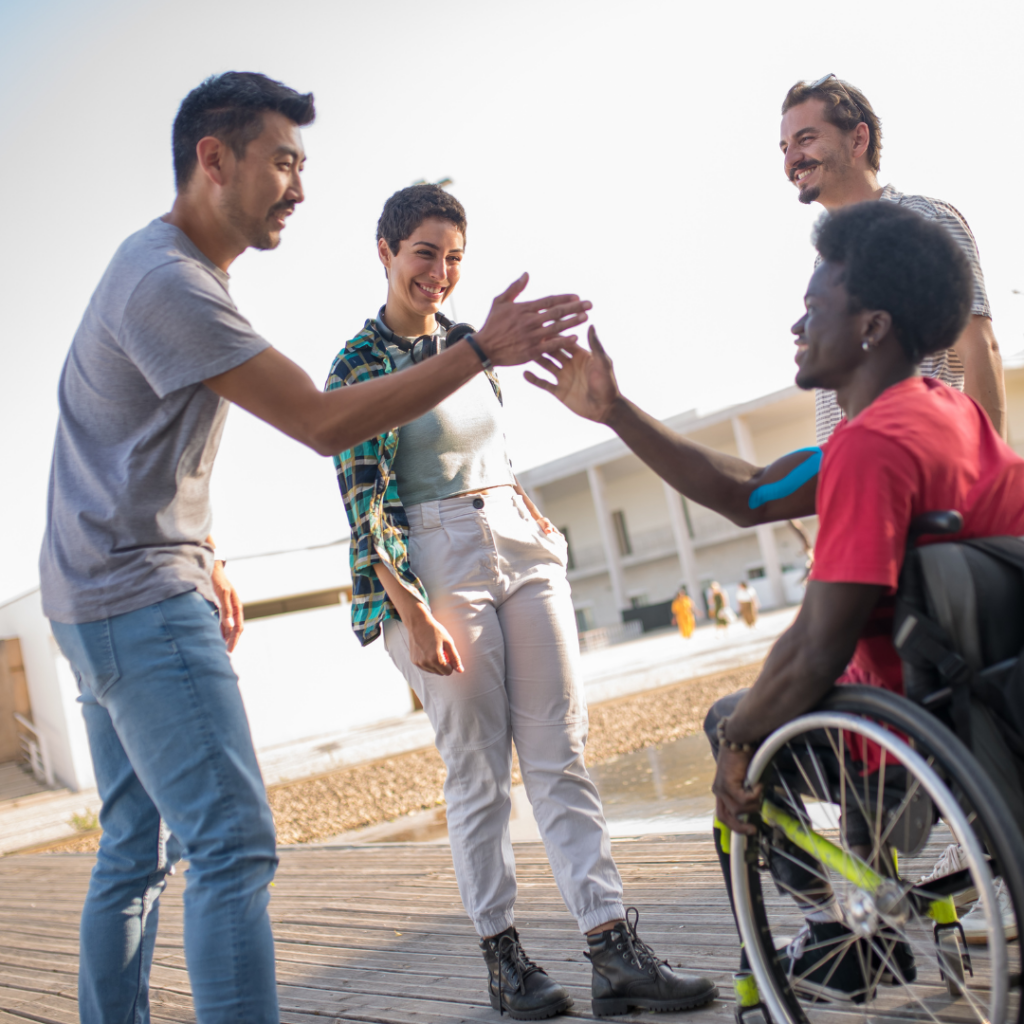 4 people outside, one guy in wheelchair high fiving another guy. 